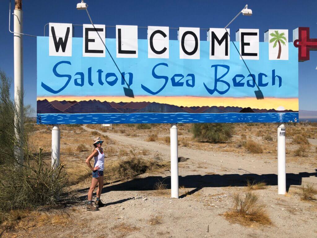 SightseeingSally standing in front of Salton Sea Beach welcome sign