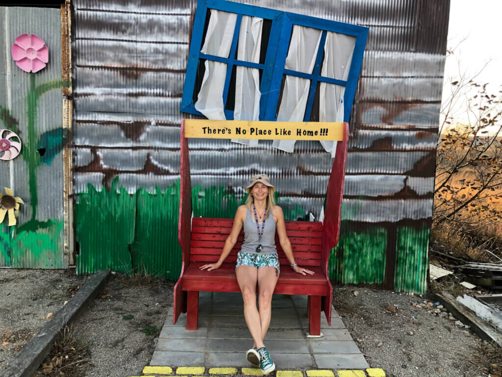 SightseeingSally sits on a red bench in front of a facade made to look like Dorothy's house from Wizard of Oz along Route 66 in Kansas.